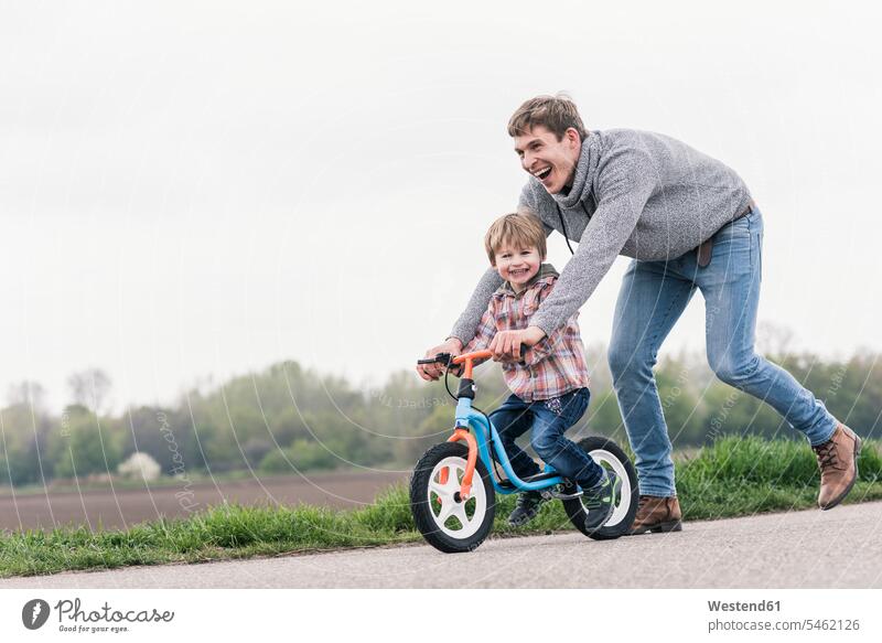 Father teaching his son how to ride a bicycle, outdoors bikes cycles bicycles learn smile play delight enjoyment Pleasant pleasure Cheerfulness exhilaration