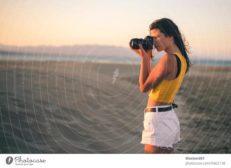 Teenage girl taking photos with camera on the beach at sunset photograph photographs sunsets sundown beaches Teenage Girls female teenagers photographing