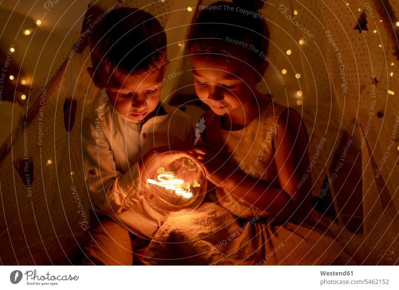 Sibling holding light while sitting in room during christmas color image colour image indoors indoor shot indoor shots interior interior view Interiors day