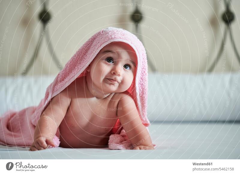 Baby girl in towel looking up while lying on bed at home color image colour image Spain indoors indoor shot indoor shots interior interior view Interiors day