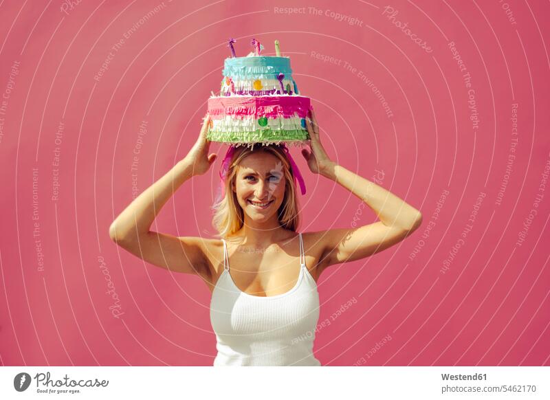 Smiling woman carrying birthday cake on head against pink wall color image colour image outdoors location shots outdoor shot outdoor shots daylight shot