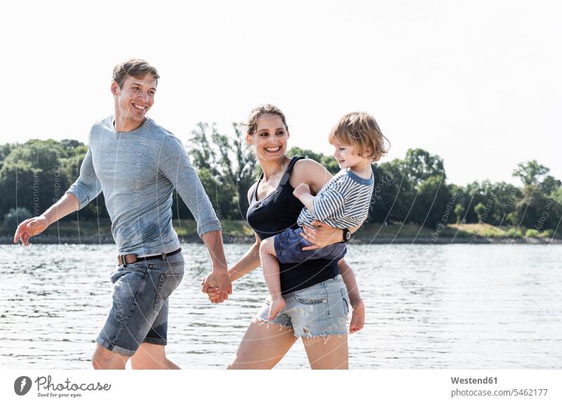 Happy family walking at the riverside on a beautiful summer day riverbank going happiness happy summer time summery summertime water's edge waterside shore