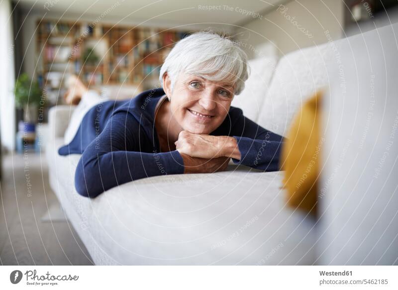Smiling senior woman with hand on chin lying on sofa at home color image colour image indoors indoor shot indoor shots interior interior view Interiors day