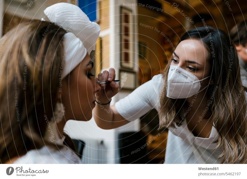Young female stylist applying make-up to bride at salon during COVID-19 color image colour image indoors indoor shot indoor shots interior interior view