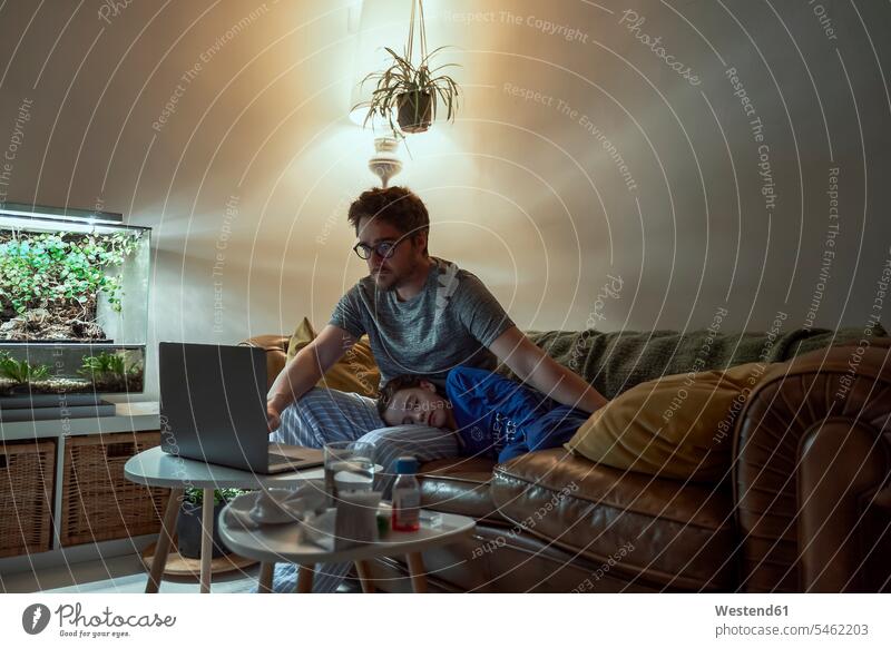 Man consulting doctor through laptop while sitting by sick daughter sleeping on sofa at home color image colour image Home Interior Home Interiors
