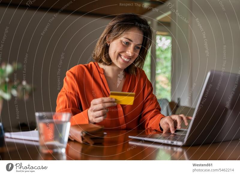 Smiling businesswoman with credit card using laptop at home color image colour image indoors indoor shot indoor shots interior interior view Interiors day