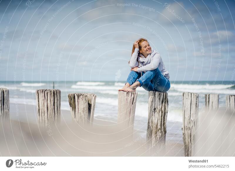 Woman sitting on fence at the beach, relaxing at the sea fences beaches woman females women relaxation relaxed ocean Seated Adults grown-ups grownups adult