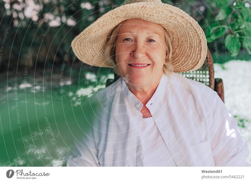Close-up of smiling senior woman wearing hat sitting on chair in yard color image colour image Spain leisure activity leisure activities free time leisure time