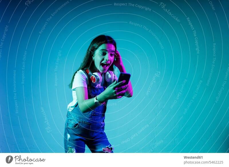 Excited girl looking at smart phone while standing against blue background color image colour image studio shot studio photograph studio photographs
