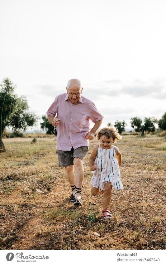 Playful grandfather with granddaughter running on land against sky color image colour image Spain leisure activity leisure activities free time leisure time