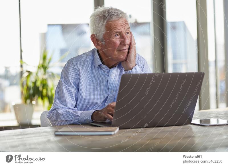 Portrait of pensive senior man sitting at table with laptop looking at distance thoughtful Reflective contemplative watching portrait portraits Seated