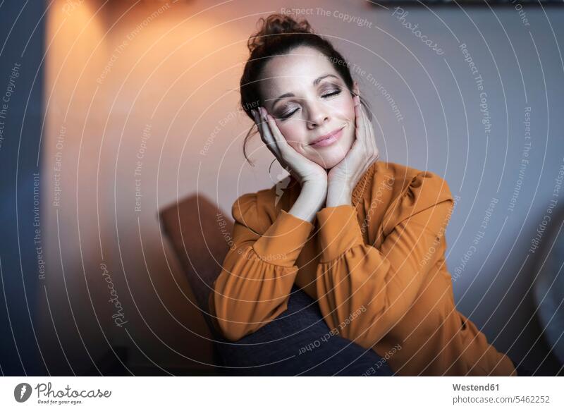 Portrait of smiling woman with closed eyes sitting on couch at home couches settee settees sofa sofas smile Seated in the evening relax relaxing relaxation