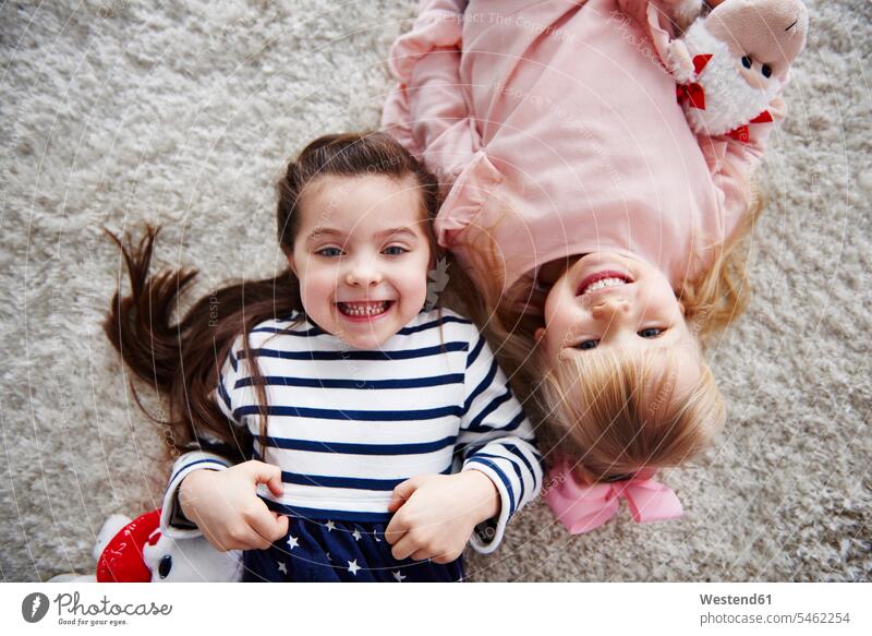 Portrait of two grinning little sisters lying on the carpet portrait portraits carpets rug rugs laying down lie lying down caucasian caucasian ethnicity