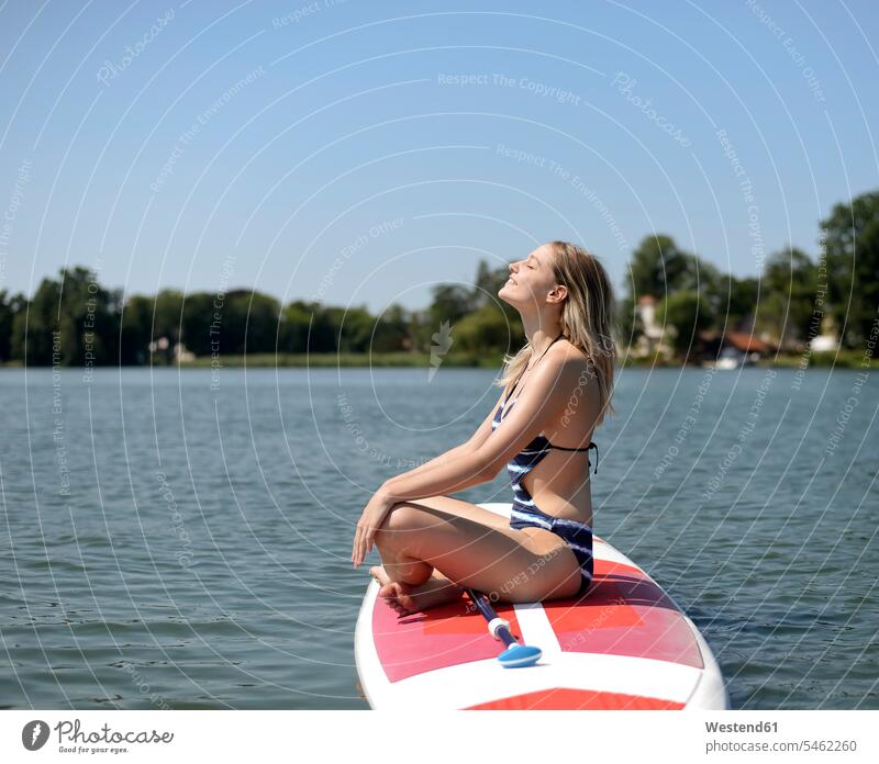 Germany, Brandenburg, woman relaxing on paddleboard on Zeuthener See sitting Seated lake lakes smiling smile Paddleboard standup paddleboard paddle board