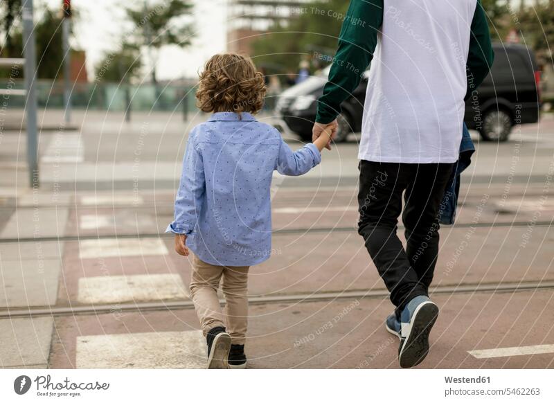 Rear view of father and son walking hand in hand in the city town cities towns pa fathers daddy dads papa sons manchild manchildren going outdoors outdoor shots