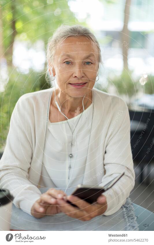 Portrait of senior woman at an outdoor cafe with cell phone and earphones senior women elder women elder woman old ear phone ear phones females smiling smile