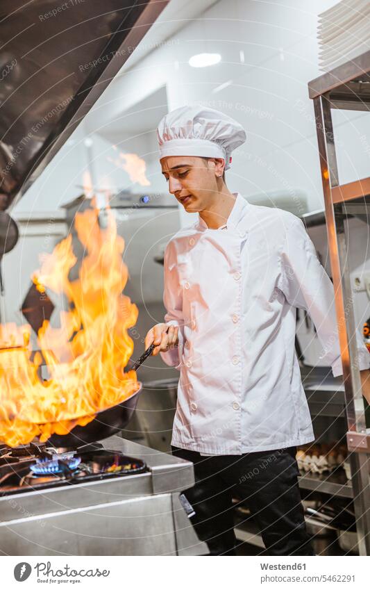 Junior chef with pan of flames in traditional spanish restaurant kitchen human human being human beings humans person persons caucasian appearance