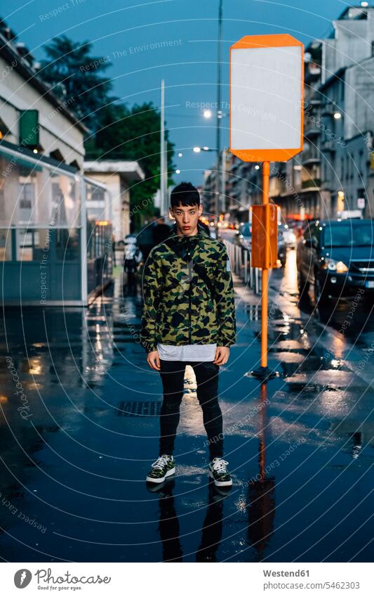 Serious man standing on wet sidewalk in city at dusk color image colour image leisure activity leisure activities free time leisure time casual clothing