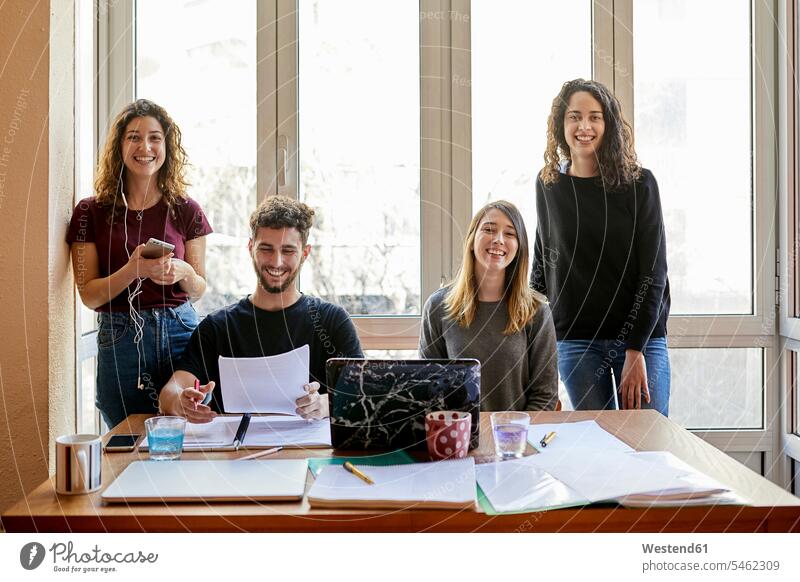 Portrait of four happy students at desk and at the window learning together desks windows happiness group of people Group groups of people higher education
