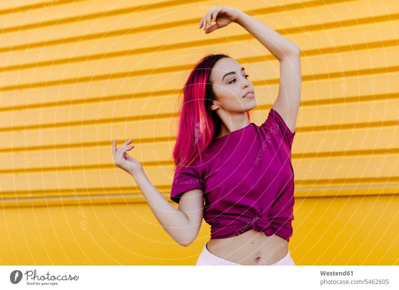 Young woman with dyed hair looking away while dancing against yellow wall color image colour image Spain leisure activity leisure activities free time