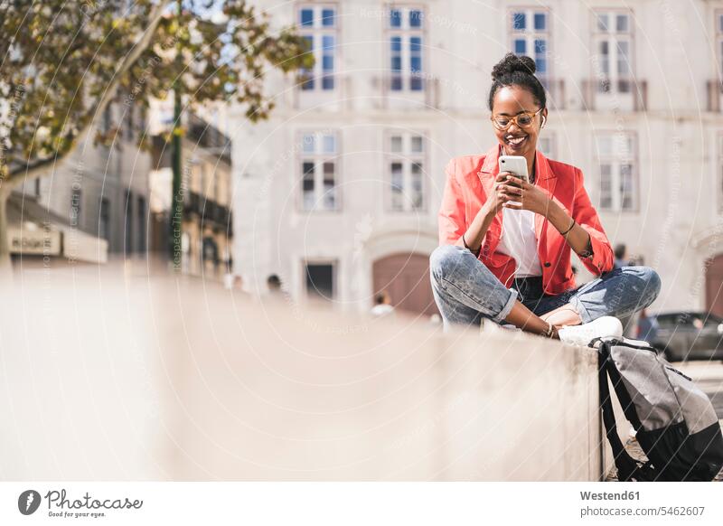 Smiling young woman with earphones and smartphone in the city, Lisbon, Portugal business life business world business person businesspeople business woman