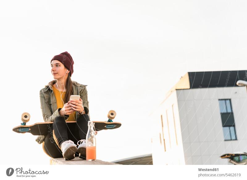 Stylish young woman with skateboard and cell phone sitting on a wall human human being human beings humans person persons caucasian appearance