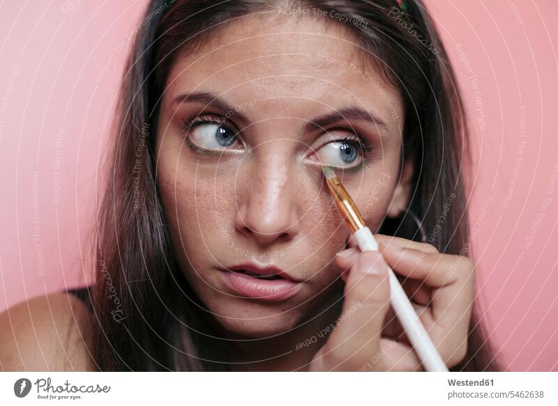 Close up of a young brunette woman with beautiful blue eyes applying eyeshadow with an eye brush differential focus blur blurred Contemporary studio shot indoor