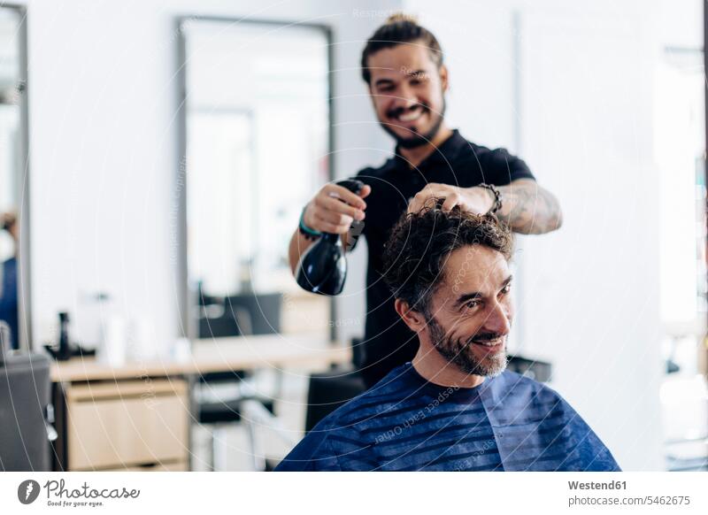 Happy hairdresser spraying water on man's hair at salon color image colour image indoors indoor shot indoor shots interior interior view Interiors day