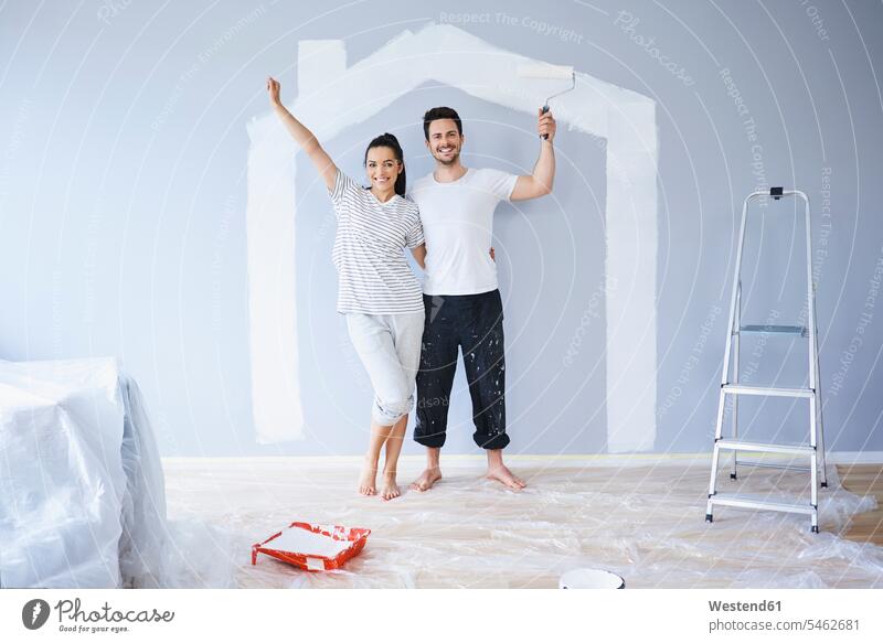 Portrait of cheerful couple painting in new apartment with house shape on wall portrait portraits shapes happiness happy gaiety Joyous glad Cheerfulness