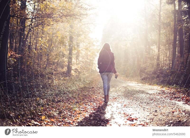 Back view of young woman walking in the woods in autumn relax relaxing seasons fall free time leisure time on the go on the road on the way solitary solo Move