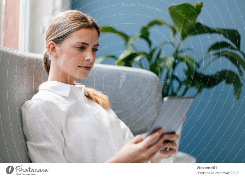 Young woman sitting on couch, using digital tablet use casual leisure wear casual clothing casual wear casual clothes Casual Attire Foliage Plant Foliage Plants