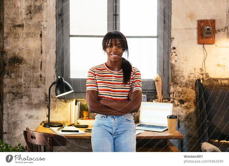 Portrait of smiling young woman standing front of desk in a loft lofts desks portrait portraits females women smile Table Tables Adults grown-ups grownups adult