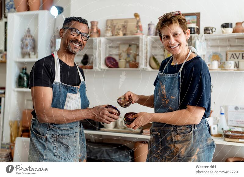 Smiling coworkers holding ceramics while standing in workshop color image colour image Spain indoors indoor shot indoor shots interior interior view Interiors
