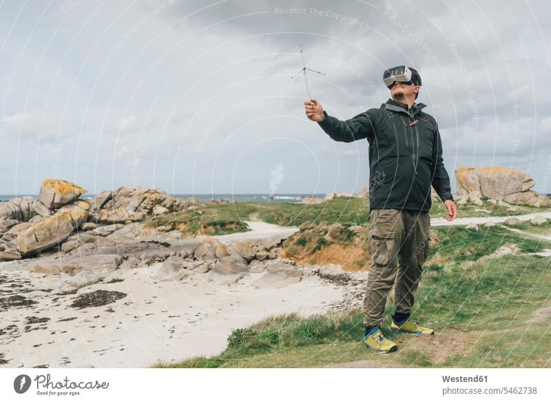 France, Brittany, Meneham, man with miniature wind turbine wearing VR glasses at the coast miniatures specs Eye Glasses spectacles Eyeglasses coastline