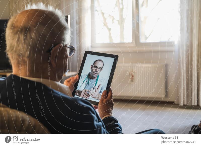 Senior man taking advice from male doctor on video call through digital tablet at home color image colour image indoors indoor shot indoor shots interior