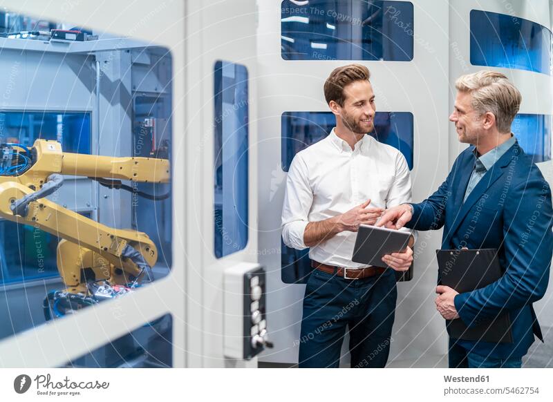 Two businessmen talking at robot in a modern factory colleague associate associates partner partners partnerships Occupation Work job jobs profession