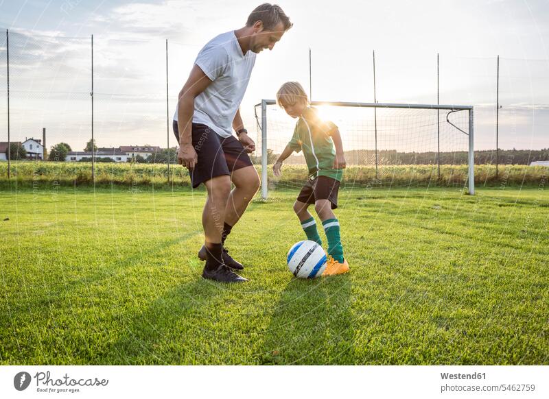 Coach and young football player on football ground at sunset boy boys males footballers football players soccer players sunsets sundown soccer pitch