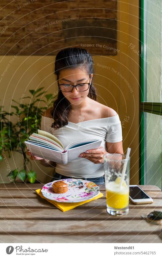 Young woman sitting at table reading a book Tables wood wood table Alimentation food Food and Drinks Nutrition human human being human beings humans person
