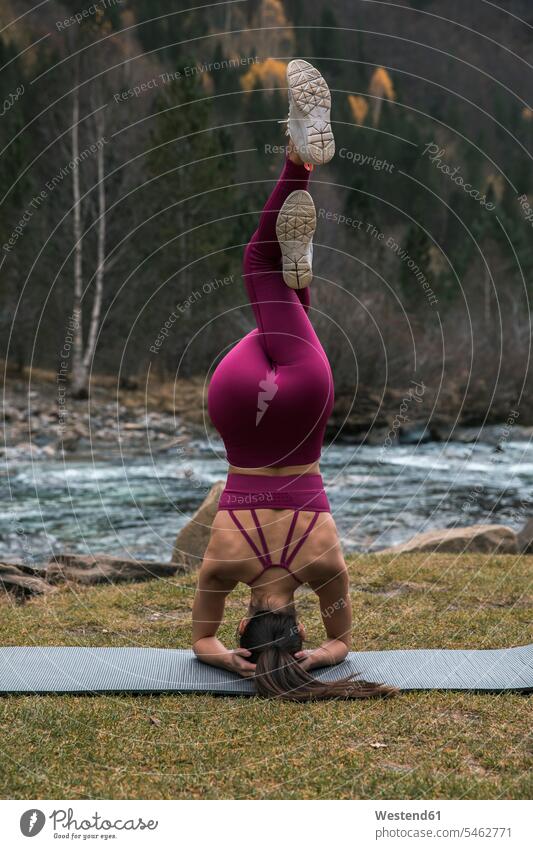 Active young woman practicing headstand pose with intertwined legs on yoga mat at Ordesa National Park, Huesca, Spain color image colour image outdoors