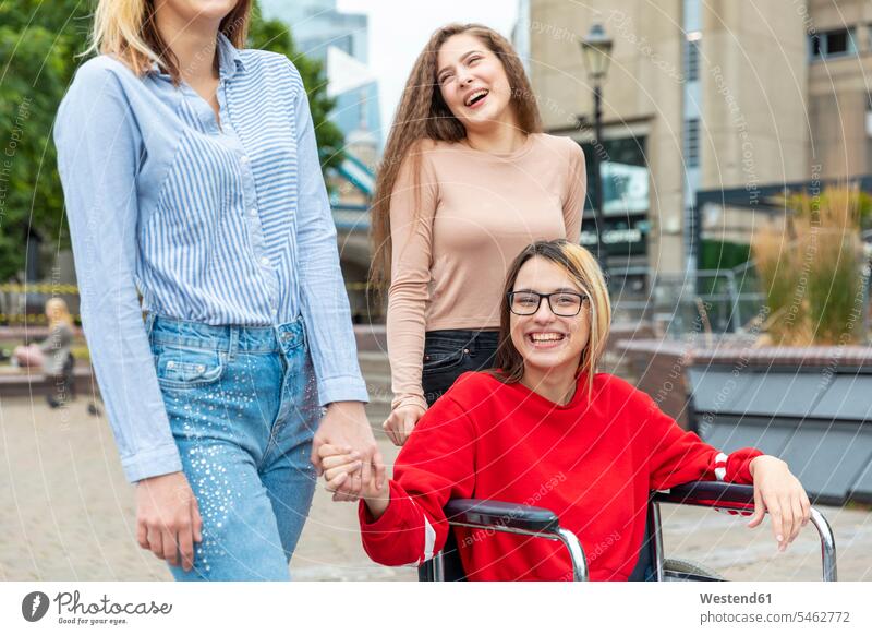 Happy disabled woman on wheelchair spending leisure time with female friends in city color image colour image outdoors location shots outdoor shot outdoor shots