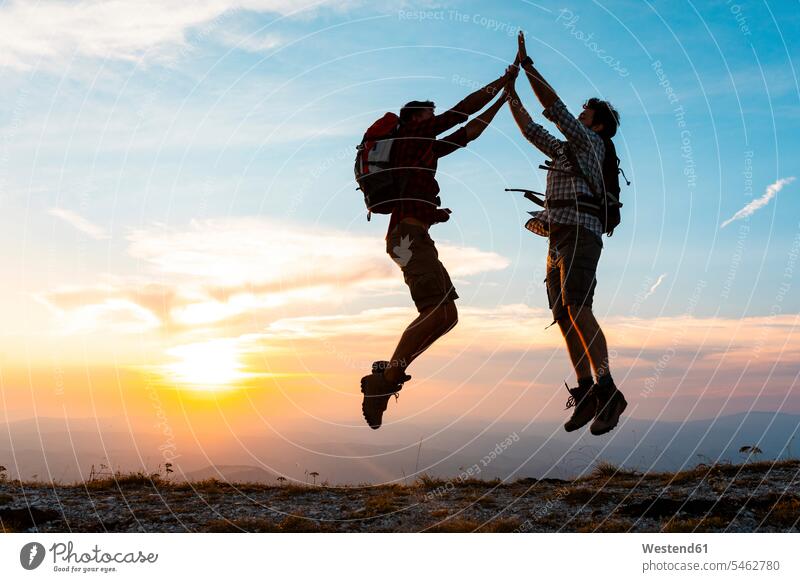 Italy, Monte Nerone, two happy and successful hikers jumping in the mountains at sunset sunsets sundown wanderers Leaping happiness mountain range