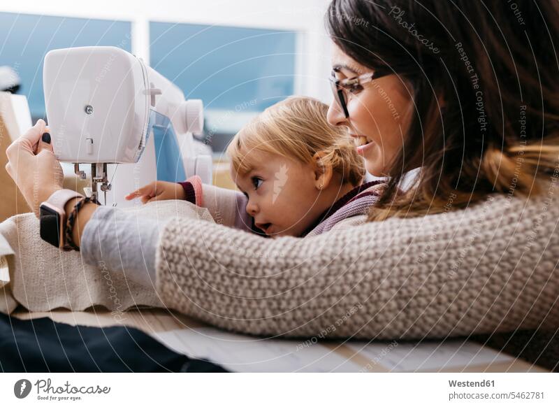 Happy mother with little daughter at home using sewing machine sewing machines mommy mothers mummy mama daughters happiness happy device devices parents family