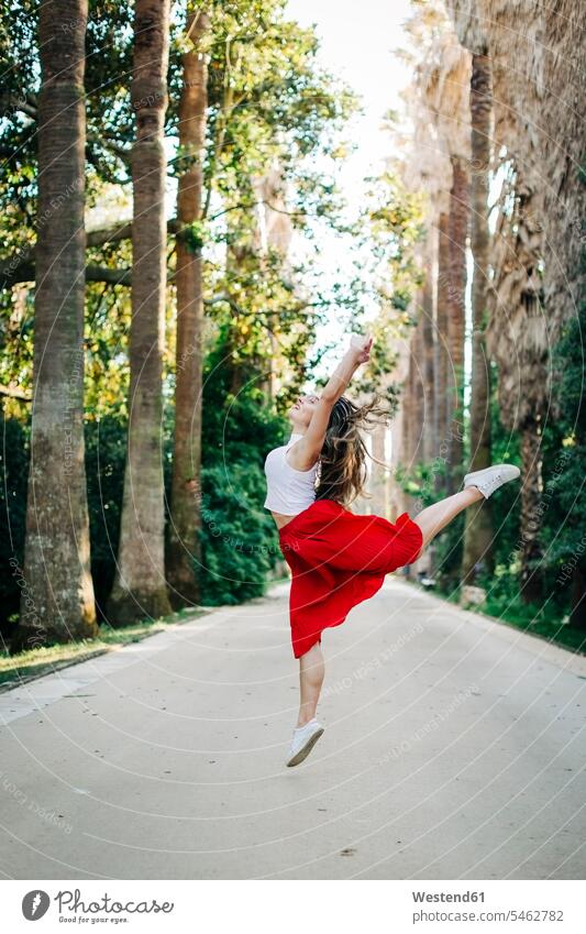 Young woman jumping while dancing on road amidst trees in park color image colour image Portugal leisure activity leisure activities free time leisure time