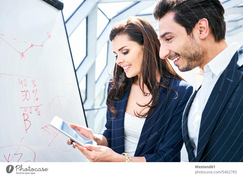 Businessman and businesswoman working with tablet and flip chart in office Business man Businessmen Business men offices office room office rooms At Work