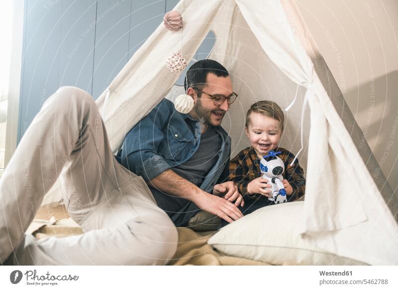 Happy father and son playing with a robot in tent at home sons manchild manchildren robots pa fathers daddy dads papa tents family families people persons