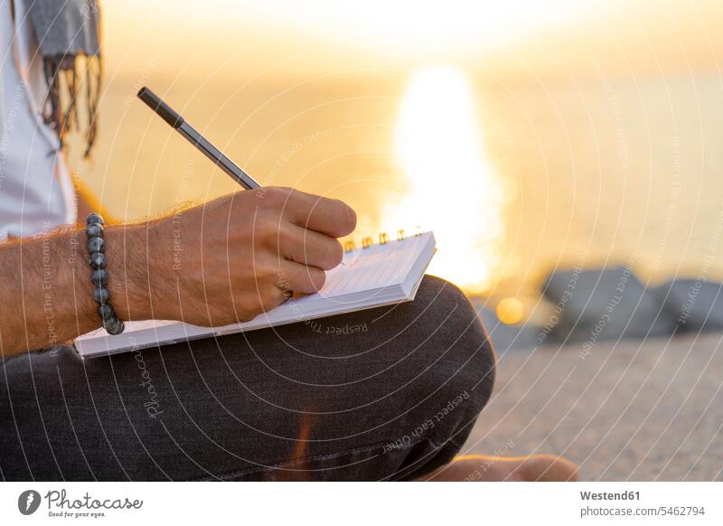 Spain. Man writing on a notebook during sunrise on rocks at the beach write writing down noting Sea ocean making a note note taking taking notes sunset sunsets