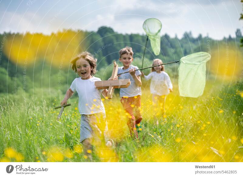 Carefree friends with model airplane and butterfly nets running on grassy land in forest color image colour image leisure activity leisure activities free time