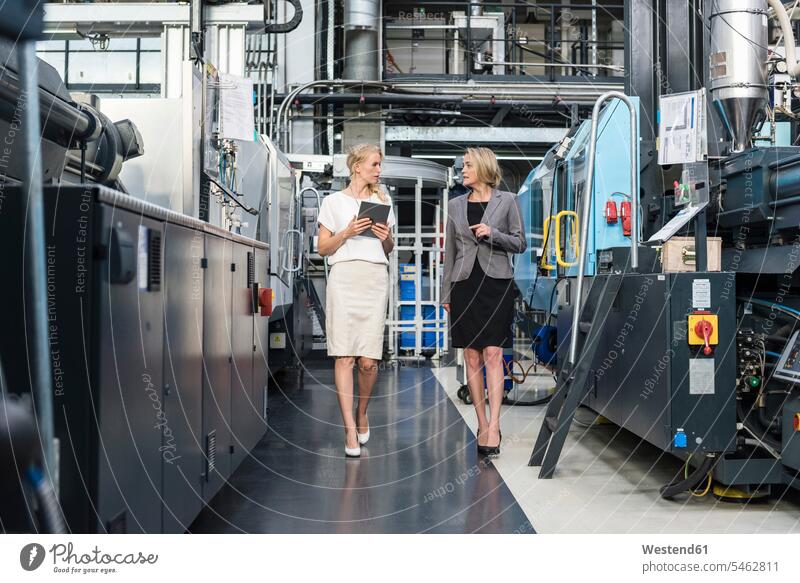 Two women with tablet walking and talking in factory shop floor industrial hall factory hall industrial buildings going speaking factories woman females
