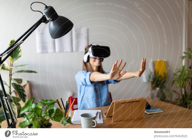 Young woman looking through virtual reality simulator gesturing while sitting in home office color image colour image Spain casual clothing casual wear