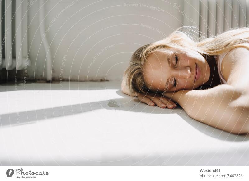 Portrait of blond young woman lying on the floor with closed eyes heater radiator smile asleep relax relaxing relaxation Contented Emotion pleased clear fair